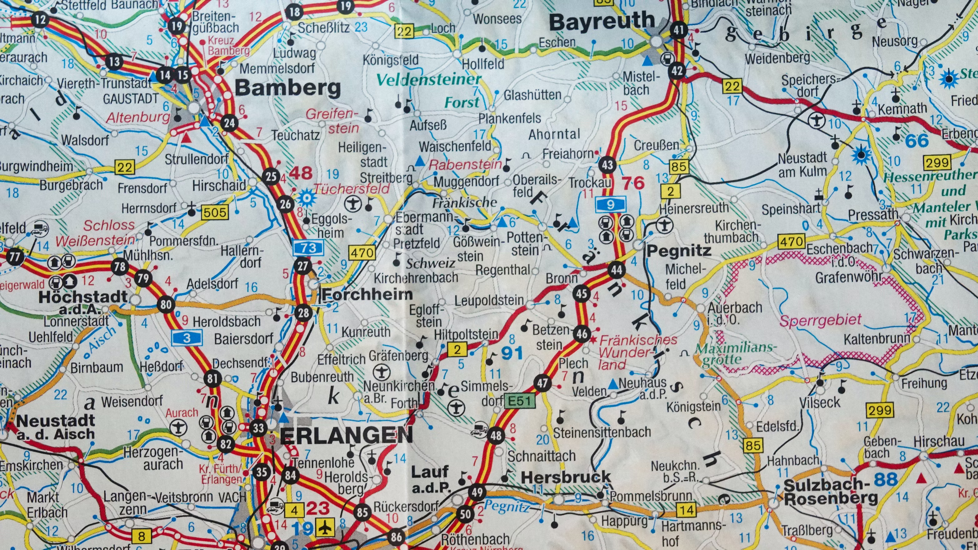 Close-up photo of a road map focusing on the Bavarian region in Germany, showing towns like Bamberg, Bayreuth, and Erlangen, with colored roads, symbols for points of interest, and geographical features such as the Veldensteiner Forst and Pegnitz river.