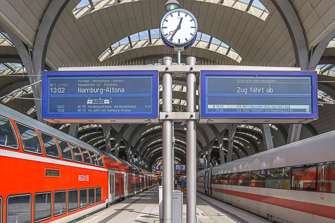 Photo taken of a train platform on the bottom level of Berlin Hbf. A double decker red train is on the left track while on the right is a smaller, single level white train. Two screens between the tracks list arrival and departure times.