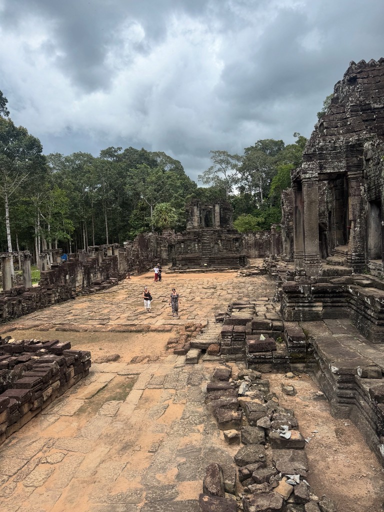 Looking across Bayon&rsquo;s courtyard toward one of the surrounding structures under a heavy sky