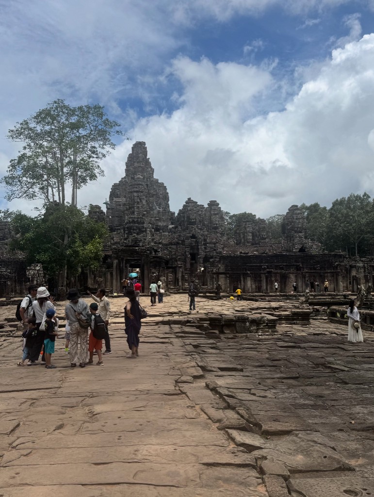 Bayon&rsquo;s courtyard opening up, several of the face towers visible at once against a partly cloudy sky