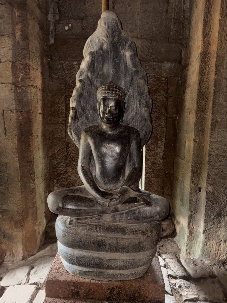 A Buddha statue seated in a niche, a carved naga hood rising behind it