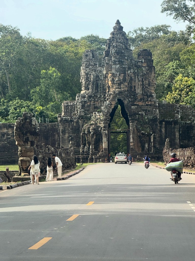 One of Angkor Thom&rsquo;s gates seen straight on from the road, the tower rising above the trees