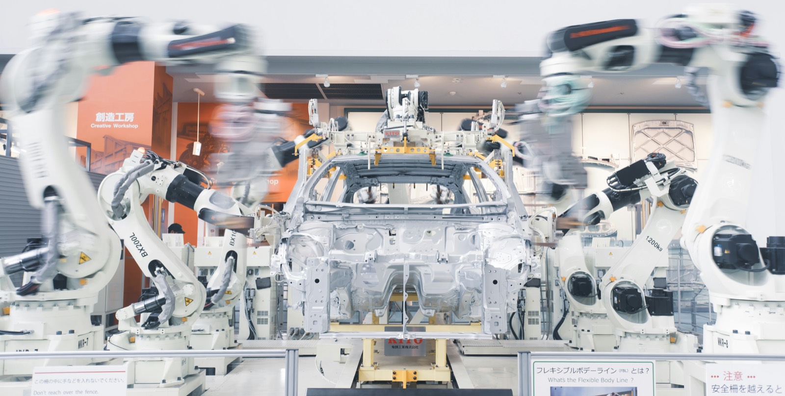 Robotic arms blurred in motion around a bare car body on an assembly line